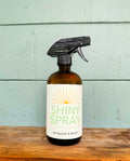 Bottle of 'Shiny Spray' with a label on a wooden surface and light blue background