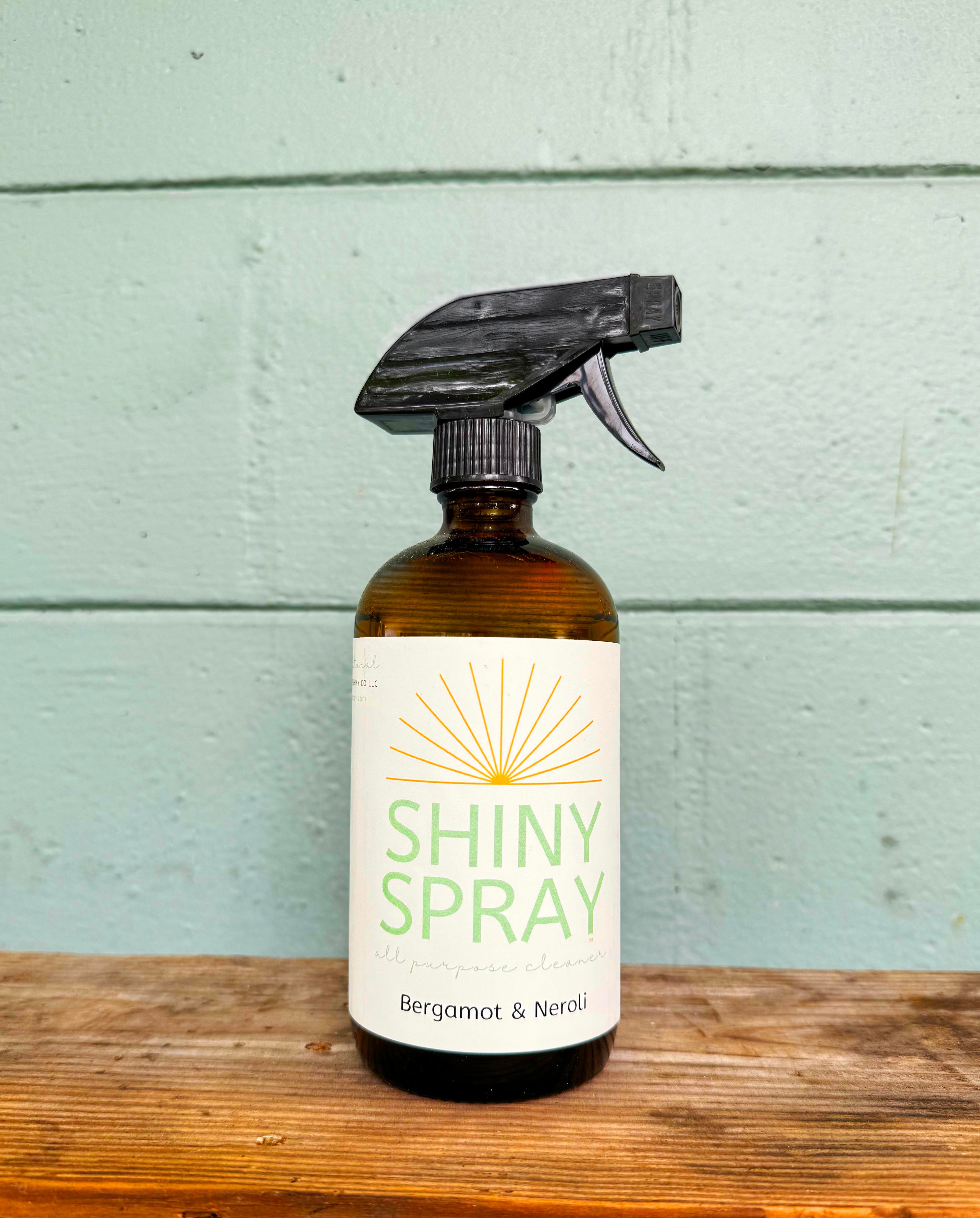 Bottle of 'Shiny Spray' with a label on a wooden surface and light blue background