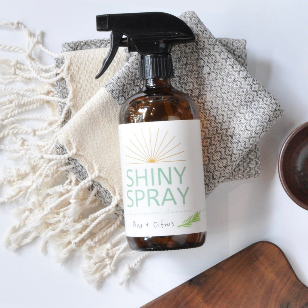 Bottle of 'Shiny Spray' with wooden bowls and a cloth on a light background